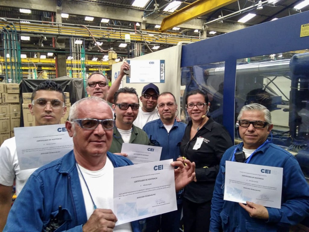 Grupo de participantes de una formación técnica del CEI junto a una máquina de inyección mostrando sus certificados.